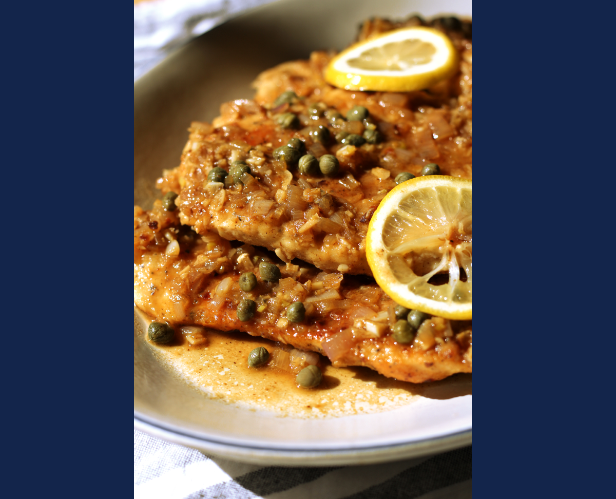 Close-up of Chicken Piccata served in a shallow bowl, topped with lemon slices, capers, and a rich, golden butter-wine sauce.