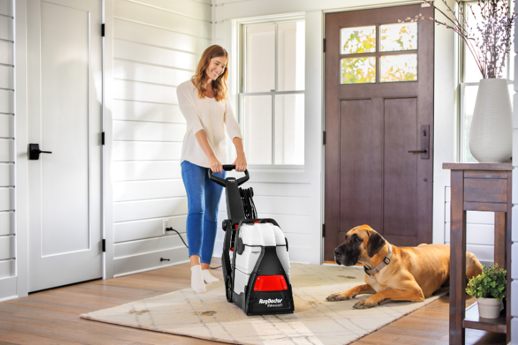Woman cleaning up a rug next to their dog.