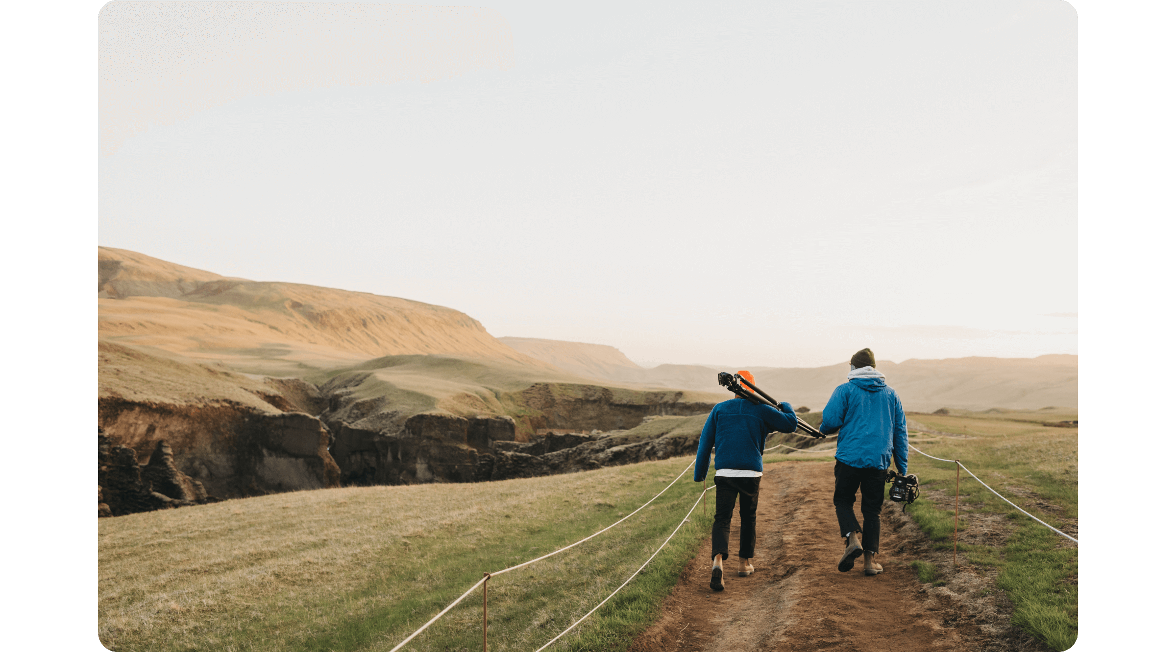 Two men walk towards a cliff in Iceland, holding a tripod and a rig