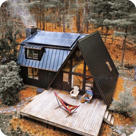 A-frame cabin with a large deck in a wooded forest.
